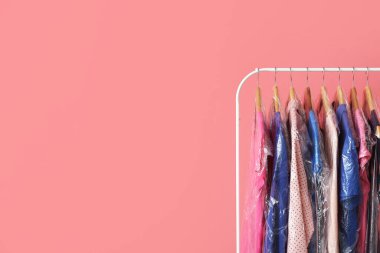 Pembe arka planda plastik poşetlerde temiz renkli giysilerle dizilin.