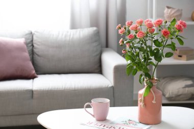 İçinde güzel taze güller ve masada bir fincan kahve olan vazo.