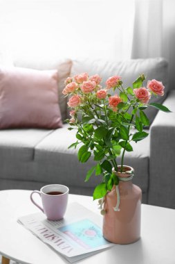 İçinde güzel taze güller ve masada bir fincan kahve olan vazo.