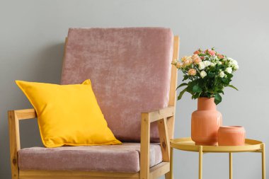 Vazo dolusu güzel taze güller ve beyaz duvarın yanında rahat bir koltuk.