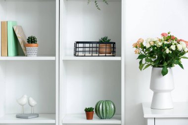 Masada bir buket güzel taze gül ve beyaz duvarın yanında dekor elementleri olan vazo.