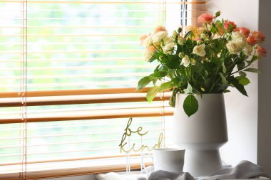 İçinde güzel taze güller ve pencere kenarında bir fincan kahve olan bir vazo.