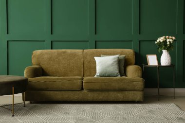 Vazo dolusu güzel taze güller ve yeşil duvarın yanında rahat bir kanepe.