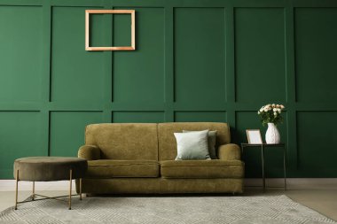 Vazo dolusu güzel taze güller ve yeşil duvarın yanında rahat bir kanepe.