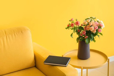 Vazo dolusu güzel taze güller ve sarı duvarın yanında rahat bir koltuk.