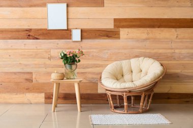 Vazoda güzel güller, masada sepet ve tahta duvarın yanında koltuk.