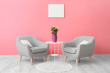 Masada mor vazodaki güller ve pembe duvarın yanındaki koltuklar.