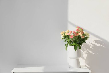 Beyaz vazo, güzel güllerle aydınlık duvarın yanında.