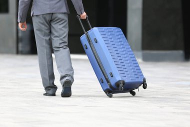 Mavi bavullu genç işadamı dışarıda yürüyor.