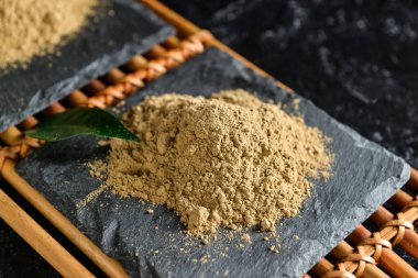 Siyah arkaplanda hojicha pudrası olan bambu hasırı, yakın plan.
