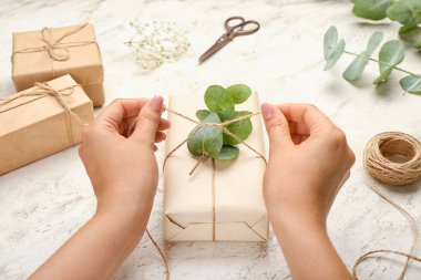 Arkaplanda okaliptüs ile hediye kutusuna halat bağlayan kadın, yakın plan.