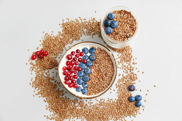Bowl and glass of sweet yogurt with flax seeds and berries on light background