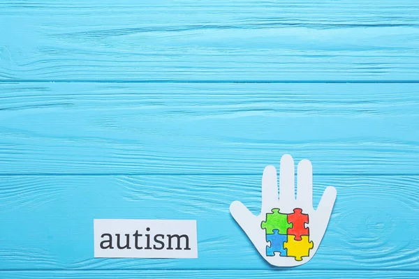 彩色木制背景下的彩色拼图和单词Autism的纸制人类手掌 — 图库照片