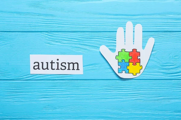 彩色木制背景下的彩色拼图和单词Autism的纸制人类手掌 — 图库照片