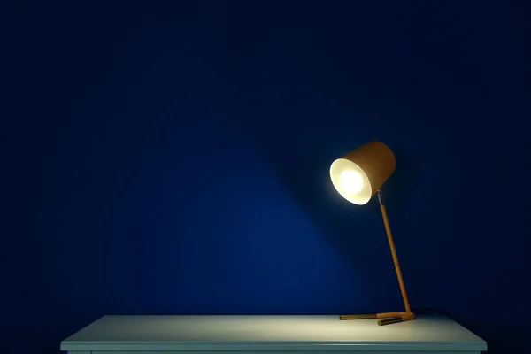 暗い部屋の青い壁の近くのテーブルの上にランプを光る — ストック写真
