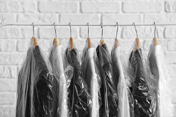 Rack Met Schone Jassen Shirts Plastic Zakken Witte Bakstenen Achtergrond — Stockfoto