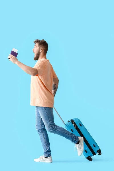 Glücklicher Junger Mann Mit Pass Und Koffer Auf Blauem Hintergrund — Stockfoto