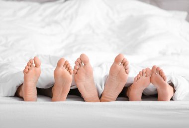 Yatakta battaniyenin altında yatan bir adam ve iki kadın. Poliyamory konsepti