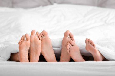 Yatakta battaniyenin altında yatan bir adam ve iki kadın. Poliyamory konsepti