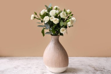 Vazo dolusu güzel güller bej duvarın yanındaki masada.