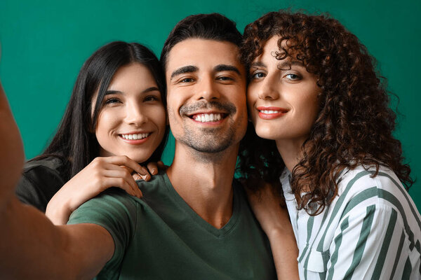 Man and two beautiful women taking selfie on color background. Polyamory concept