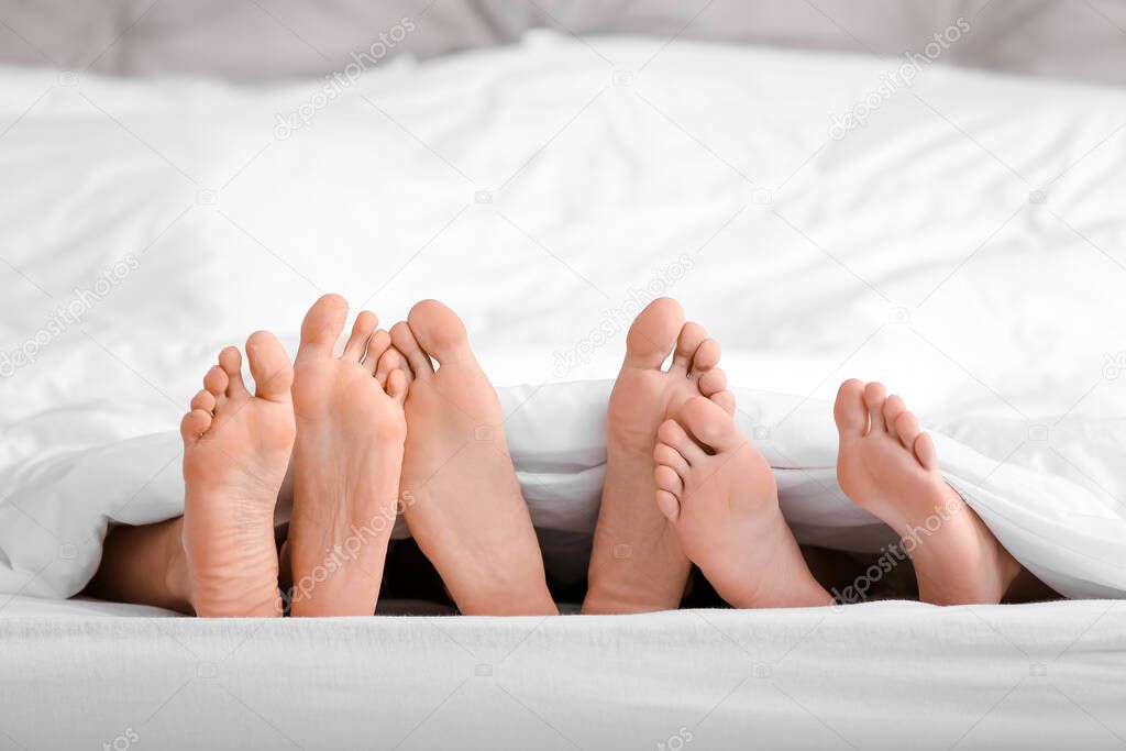 Feet of man and two women lying under blanket in bed. Polyamory concept