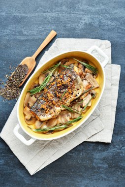 Gri zemin üzerinde levrek, mantar ve biberiye dalları olan bir yemek tabağı.