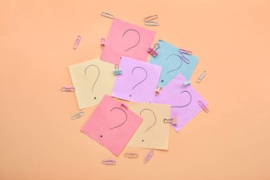 Kağıt, bej arka planda soru işaretleri ve ataçlarla yapışır.