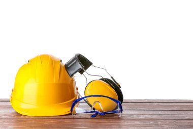Güvenlik kasketi ve koruyucu kulaklık, beyaz arka planda, tahta masada gözlüklü.