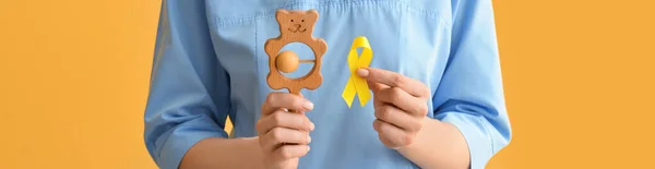 Female Nurse Holding Golden Awareness Ribbon Baby Rattle Color Background — Stock Photo, Image