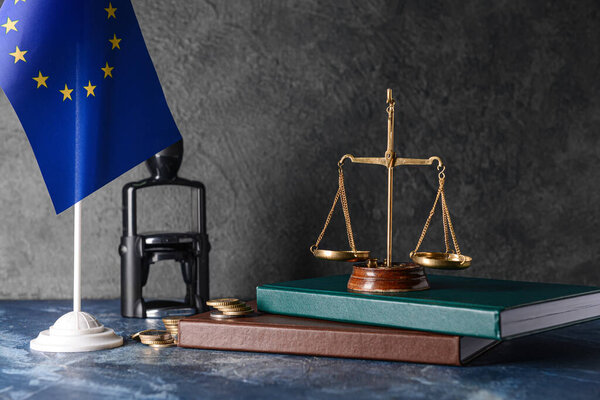 Scales of justice with books, coins and European Union flag on dark background