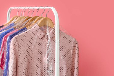 Pembe arka planda plastik poşetlerde temiz renkli kıyafetlerle dizilin.