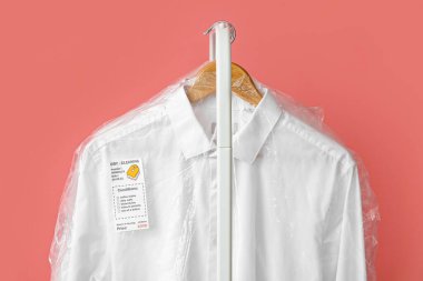 Temiz beyaz gömlekleri pembe arka planda plastik poşetlerle dizin, yakın plan.