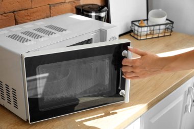 Modern mikrodalga fırını tuğla duvarın yanındaki tahta tezgaha kapatan kadın.