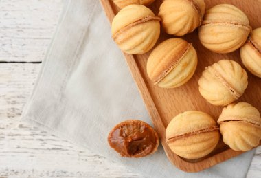 Hafif ahşap zemin üzerinde kaynamış konsantre süt ile lezzetli ceviz şeklinde kurabiyeler, yakın plan.