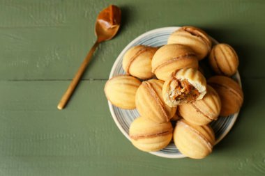 Ahşap arka planda kaynatılmış konsantre sütle lezzetli ceviz şekilli kurabiyeler.