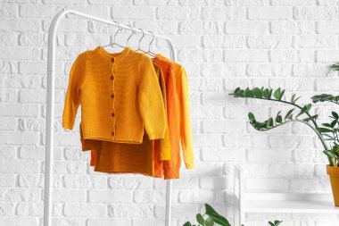 Beyaz tuğla duvarın yanında süveter ve çiçek askısı.