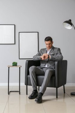 Şık takım elbiseli yakışıklı adam koltukta oturuyor ve saati kontrol ediyor.