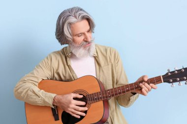 Mavi arka planda gitar çalan son sınıf öğrencisi sakallı.