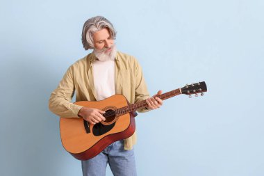 Mavi arka planda gitar çalan son sınıf öğrencisi sakallı.