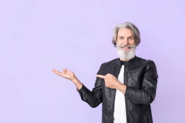 Deri ceketli yaşlı adam leylak arka planda bir şeye bakıyor.