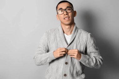 Gri arka planda örgü süveter giyen yakışıklı Asyalı genç adam.