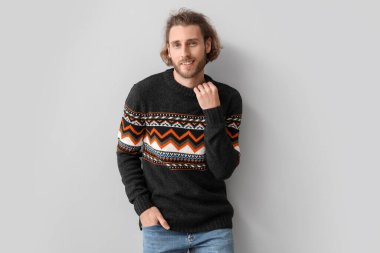 Gri arka planda örülü süveter giyen yakışıklı genç adam.