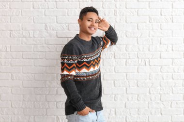 Beyaz tuğla arka planda örgü kazak giyen yakışıklı Afro-Amerikalı adam.