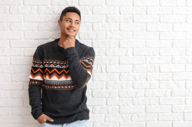 Beyaz tuğla arka planda örgü kazak giyen yakışıklı Afro-Amerikalı adam.