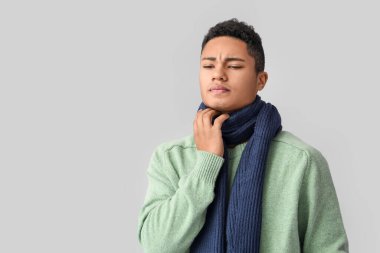 Gri arka planda boğazı ağrıyan Afro-Amerikalı bir adam.