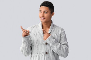 Örgü kazaklı yakışıklı Afro-Amerikalı adam açık arkaplanlı bir şeyi işaret ediyor.