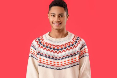 Kırmızı arka planda örgü süveter giyen yakışıklı Afro-Amerikalı adam.