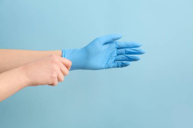 Mavi arka plana tıbbi eldiven takan kadın.