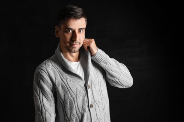 Esmer arka planda örülü süveter giyen yakışıklı bir genç.